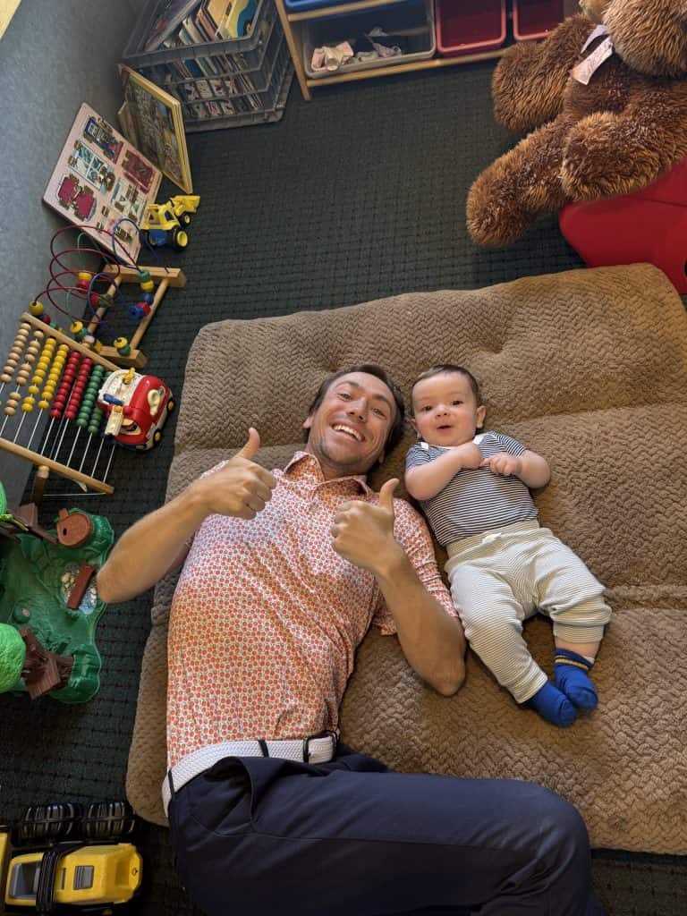 Dad playing on the floor with the toddler surrounded by toys
