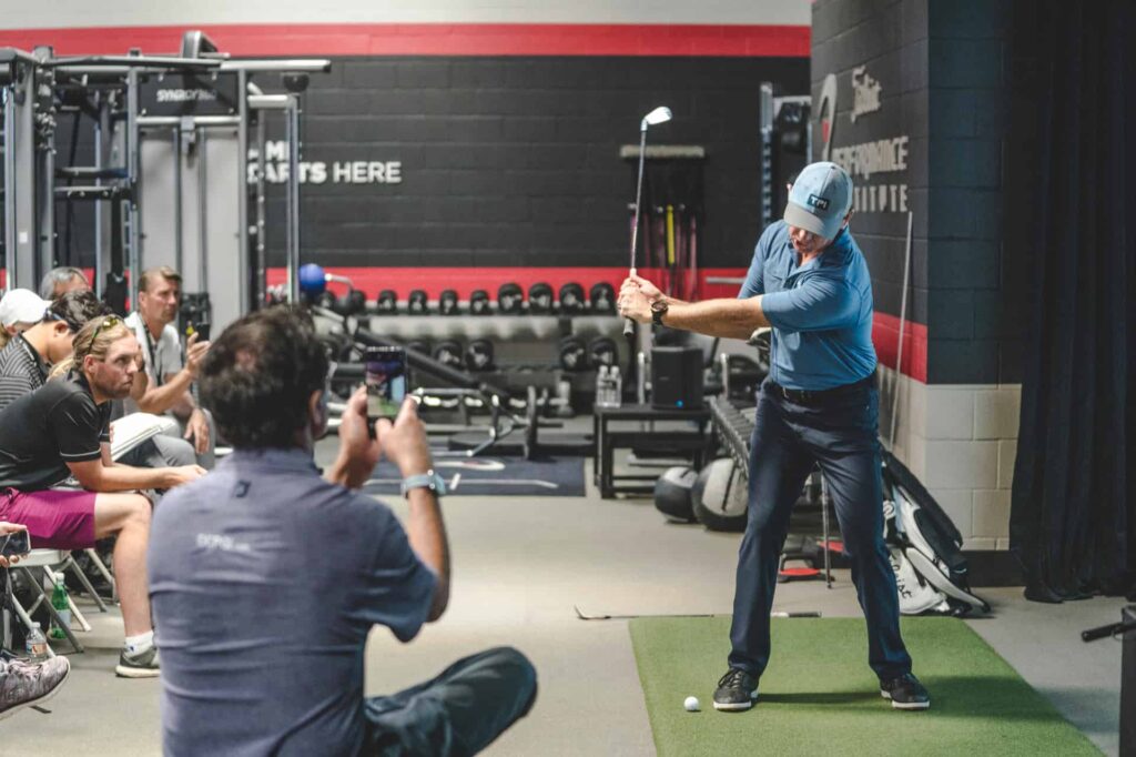 Chiropractor demonstrating golf swing mechanics during a sports performance and mobility assessment session
