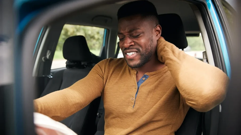 Black man holding neck in pain sitting in a car after an auto accident